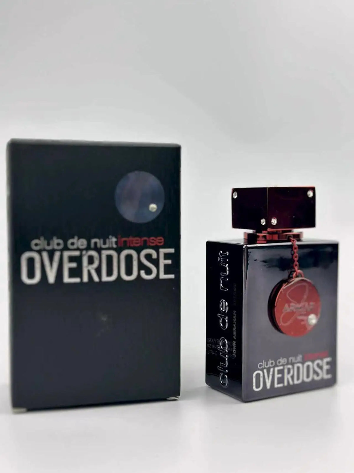 A dark red and black perfume bottle and its rectangular box set against a blurry white background.