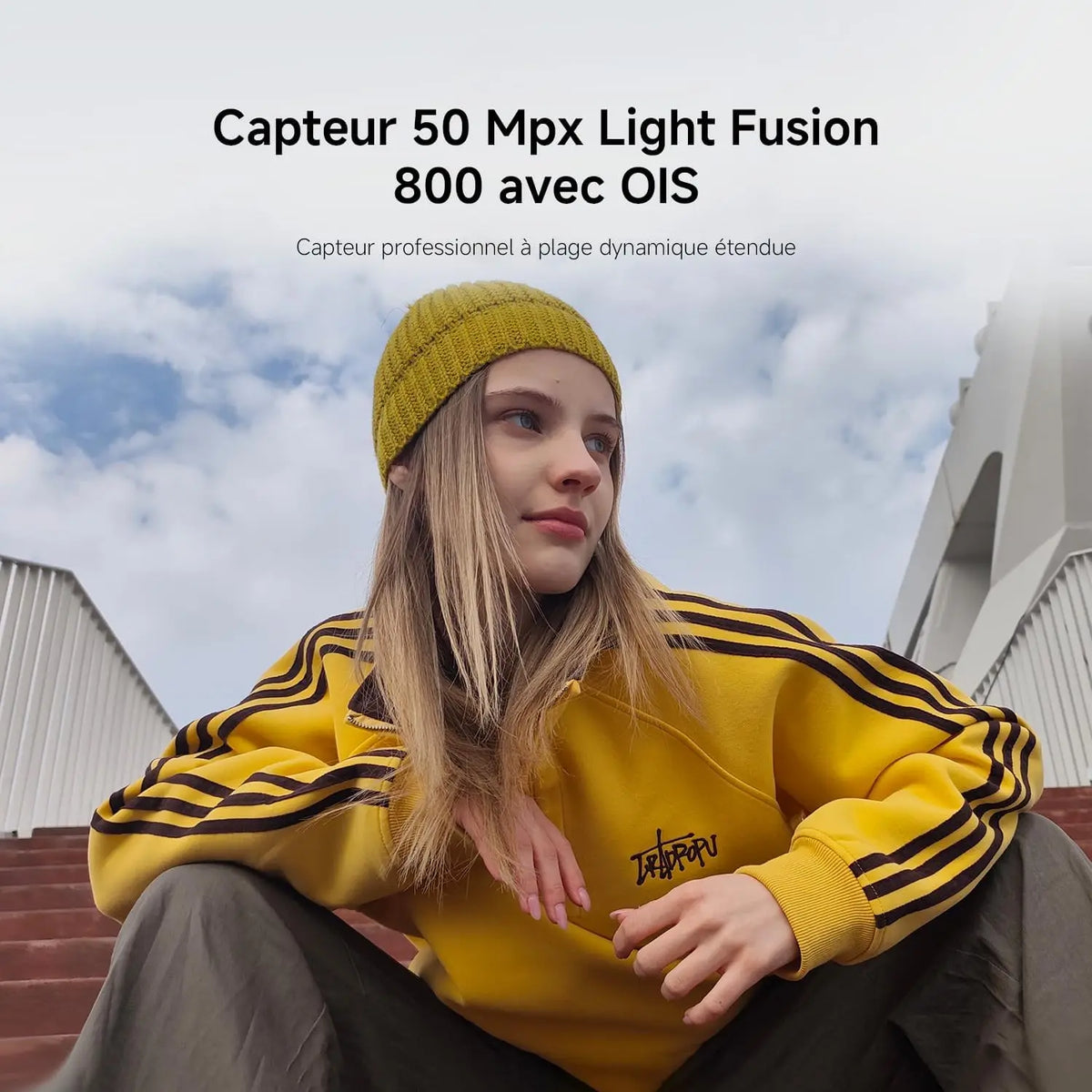 A woman wearing a yellow beanie and sweatshirt sitting on outdoor stairs.