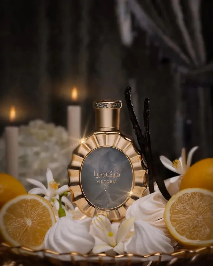 Golden perfume bottle surrounded by vanilla beans, lemon slices, and white flowers.