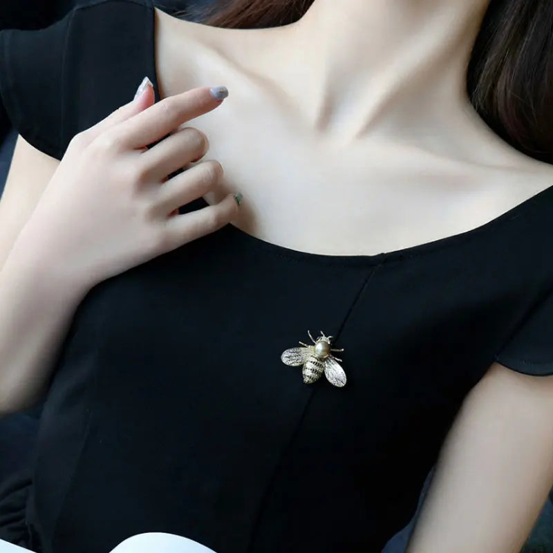 Close-up of a person wearing a bee brooch on a black dress.