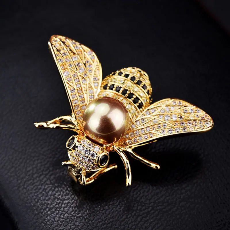 Gold-toned bee brooch with a large central pearl, black and yellow crystals, and pave rhinestone wings.