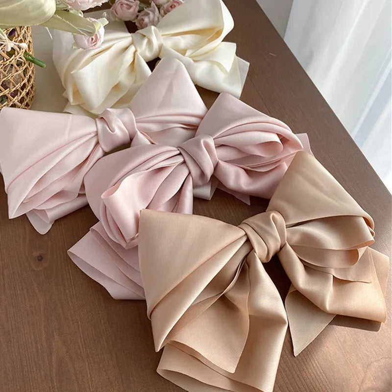 A set of four pastel-colored satin bow hair clips layered on a wooden surface