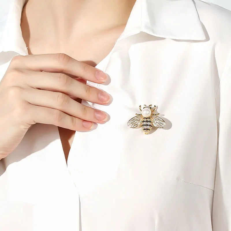 Woman wearing a gold bee brooch on a white button-down shirt.