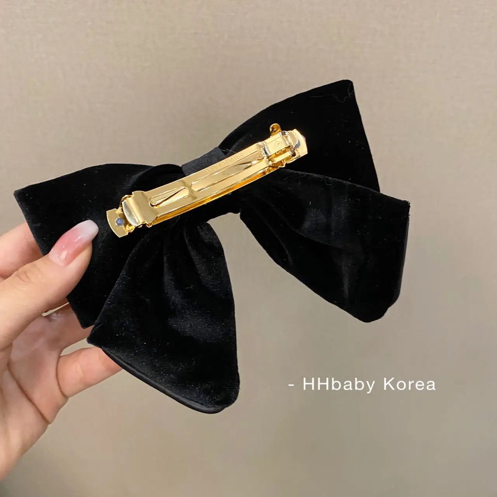 Hand holding a black velvet bow hair clip with a gold metal barrette