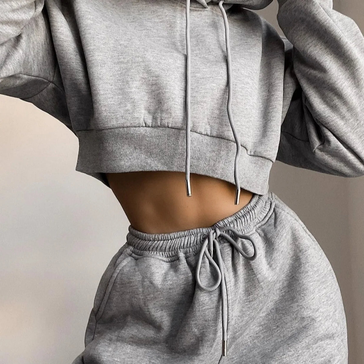 A woman wearing a grey cropped hoodie and matching grey sweatpants jogger set