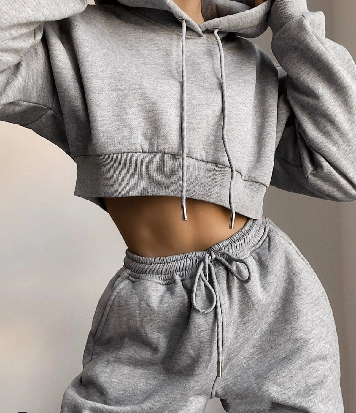 A woman wearing a light grey cropped hoodie and matching light grey sweatpants jogger set