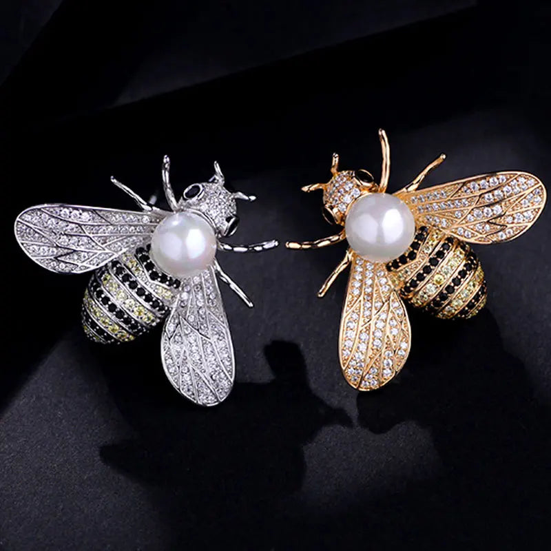 Two bee-shaped brooches in silver and gold tone, each featuring a pearl center and crystal embellishments.