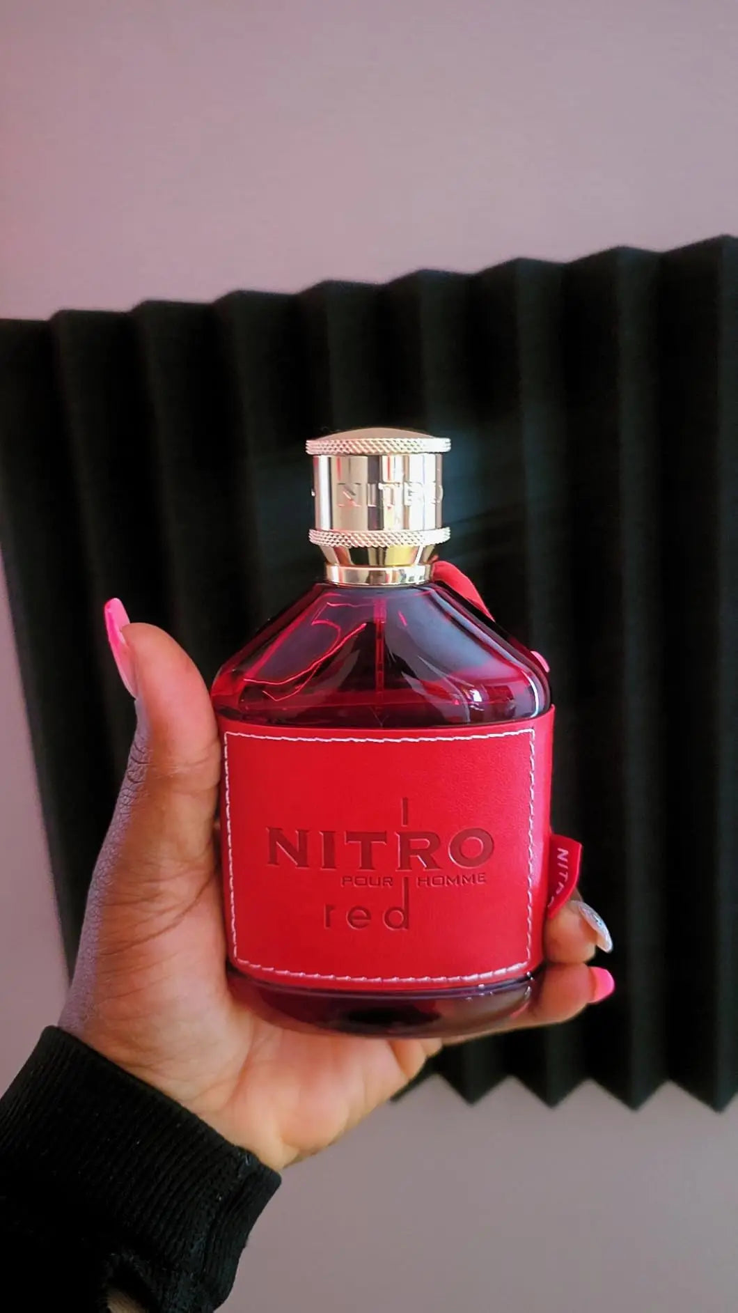 A hand holding a red perfume bottle against a dark grey background.