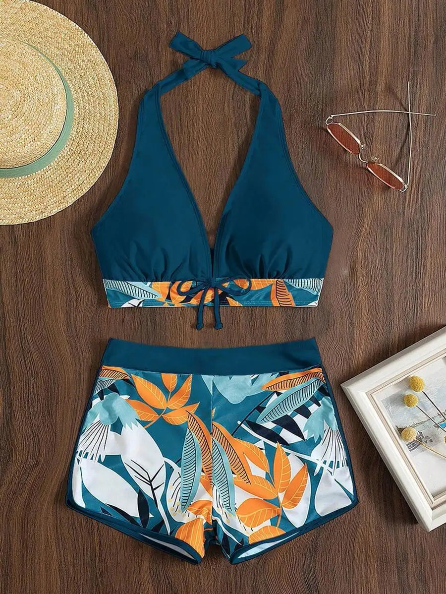 Blue halter bikini set with tropical leaf pattern, straw hat and sunglasses on wooden background