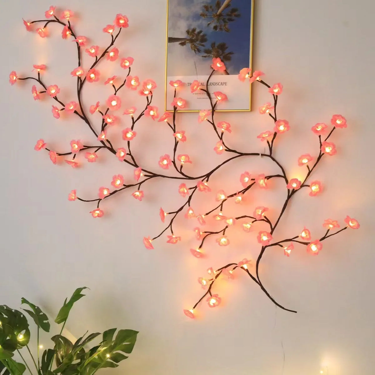 Pink cherry blossom vine string lights wall decor next to framed picture and houseplant