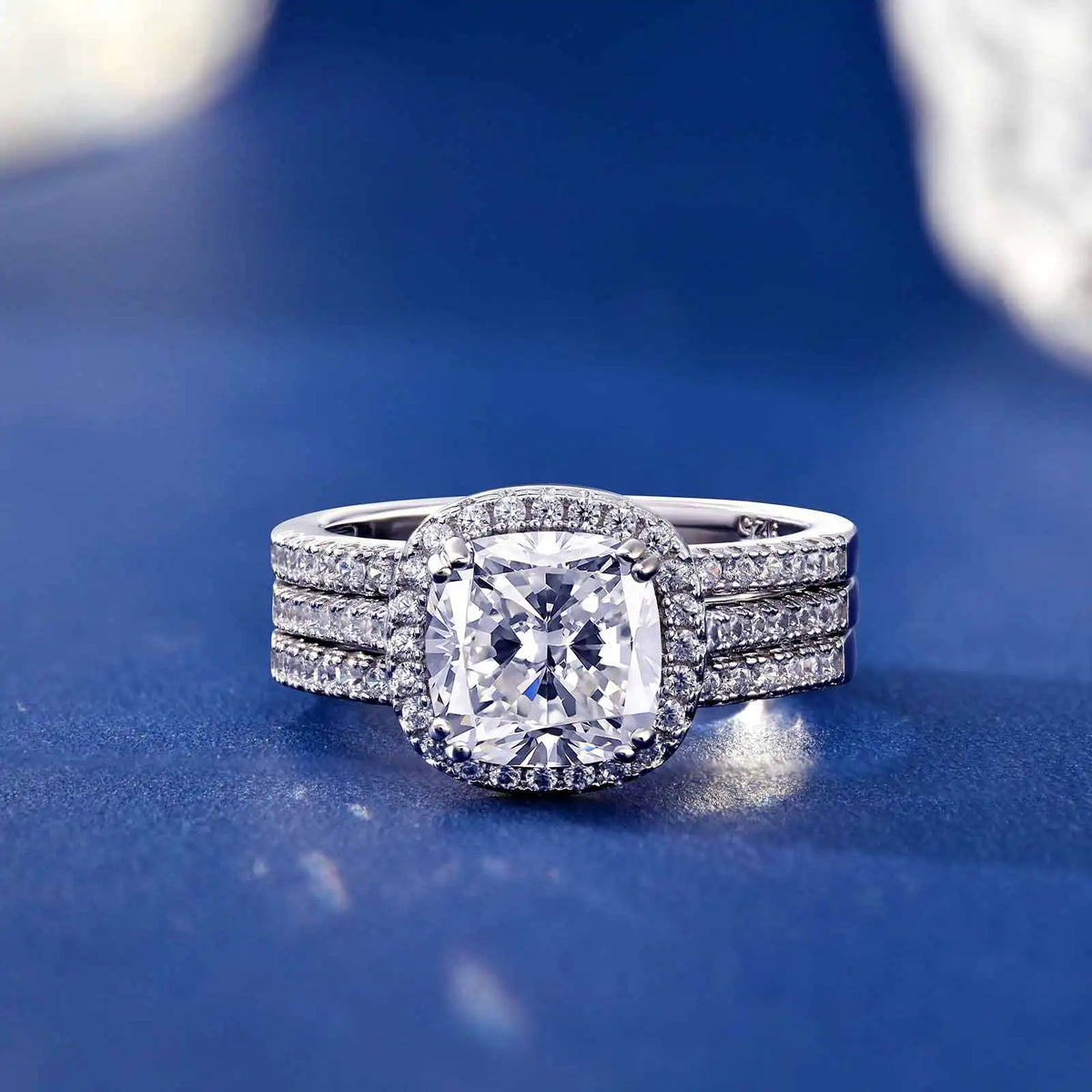 Three-piece cushion cut halo engagement ring set on a deep blue background