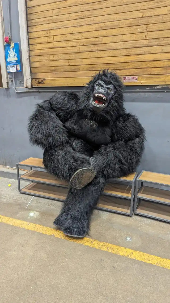 A black king kong mascot costume sitting on a wooden bench.