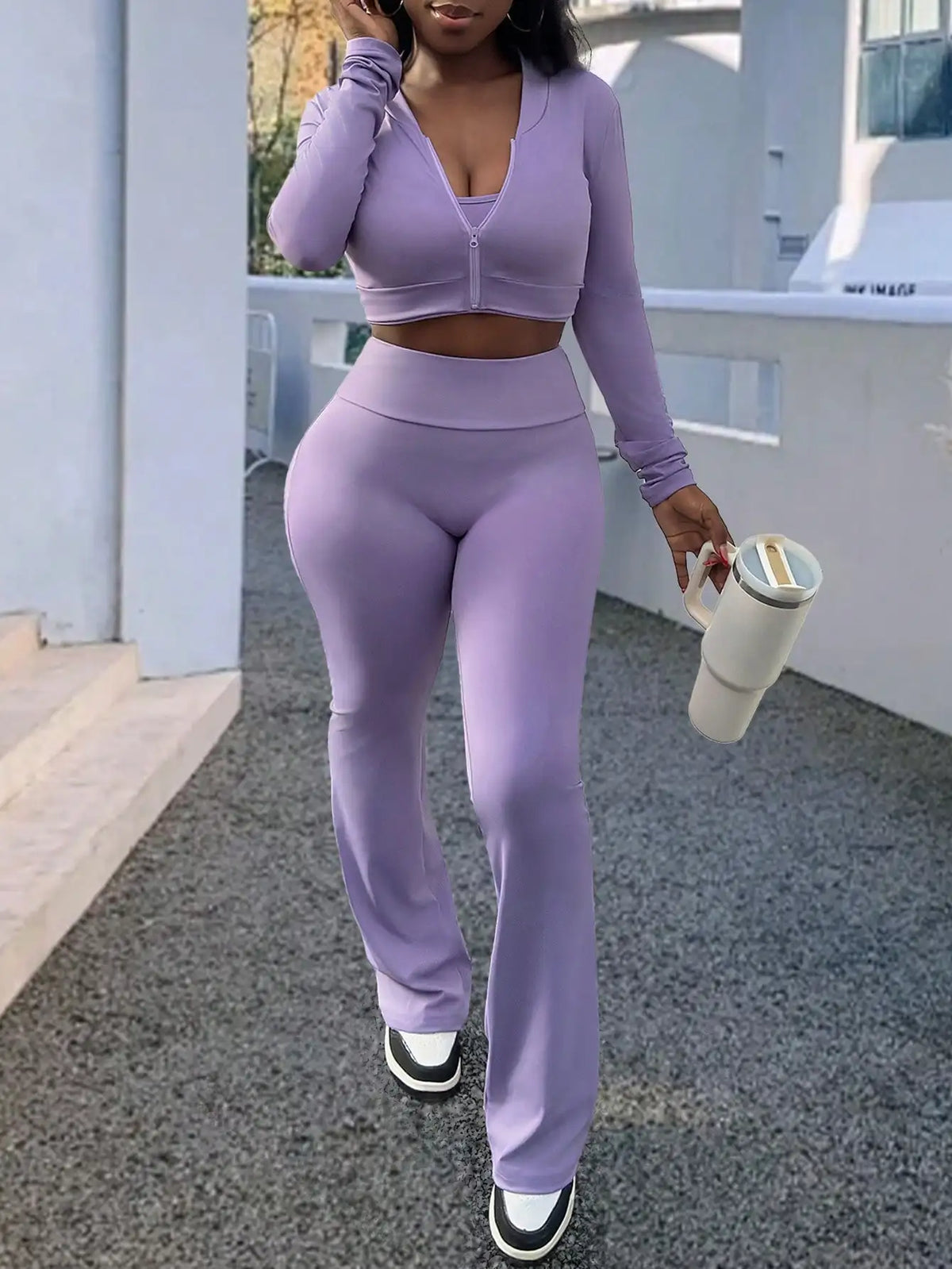 A woman wearing a purple long-sleeve zip-up top and matching flared trousers, holding a large tumbler cup.
