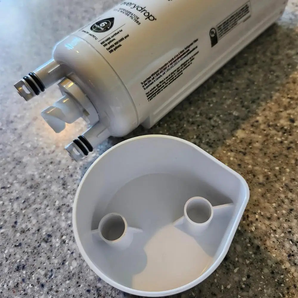 Bottom view of a white refrigerator water filter showing inlet ports and rubber gaskets