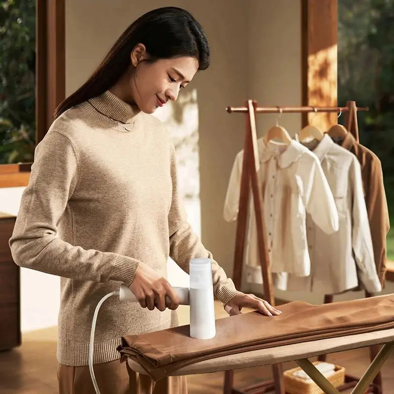 Woman using a white handheld garment steamer on clothing.