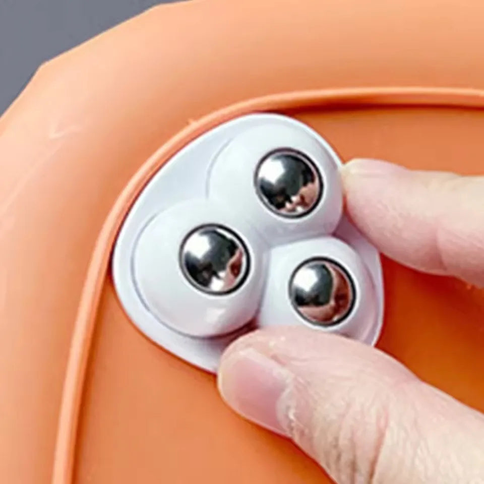 Close-up of a white triangular adhesive universal wheel with stainless steel balls being held by a hand.