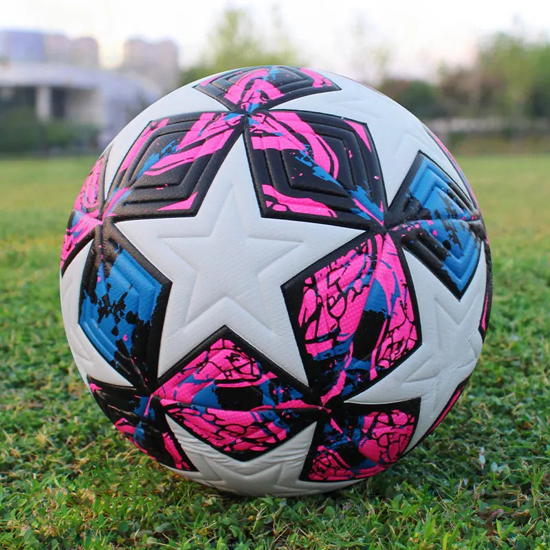 A soccer ball with a white star and pink and blue abstract design on a green field