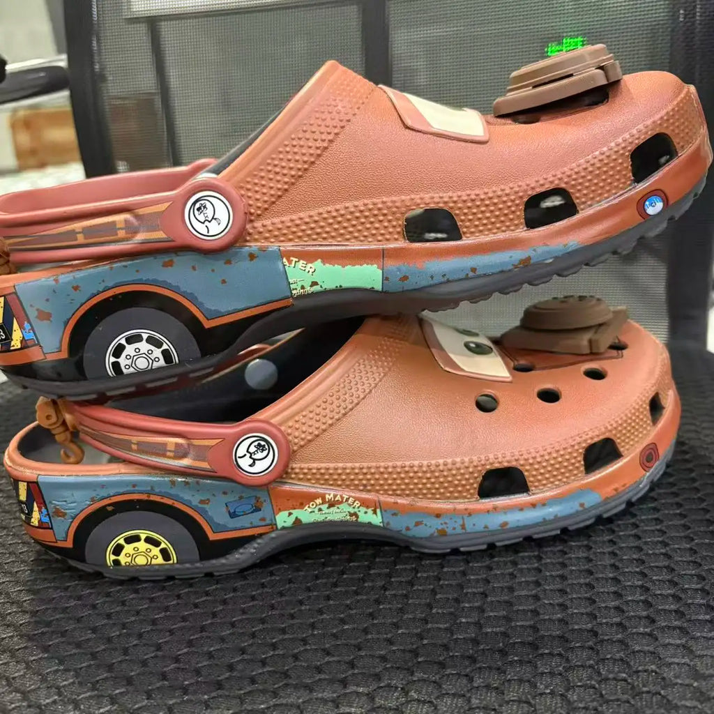 Stack of two brown cartoon tow truck themed clogs showing side graphics and engine charms.