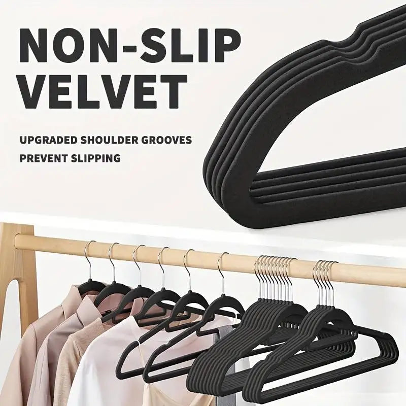 Black velvet clothes hanger with shoulder grooves on a clothing rack.