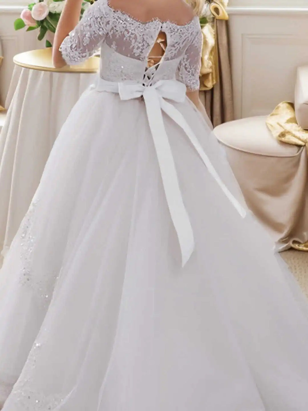 Back view of a white off-shoulder lace and tulle ball gown dress with a corset lacing and large bow.