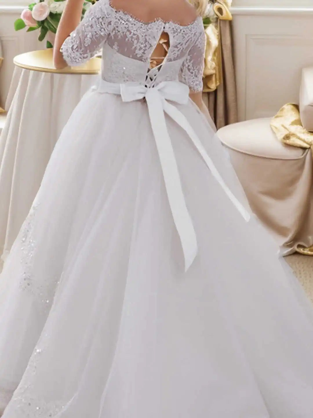 Back view of a white off-shoulder lace and tulle ball gown dress with a corset lacing and large bow.