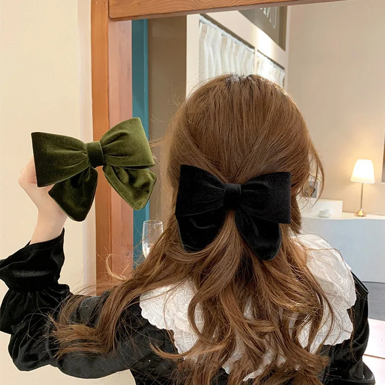 Woman with long brown hair wearing a black velvet bow clip with an extra olive green bow in hand