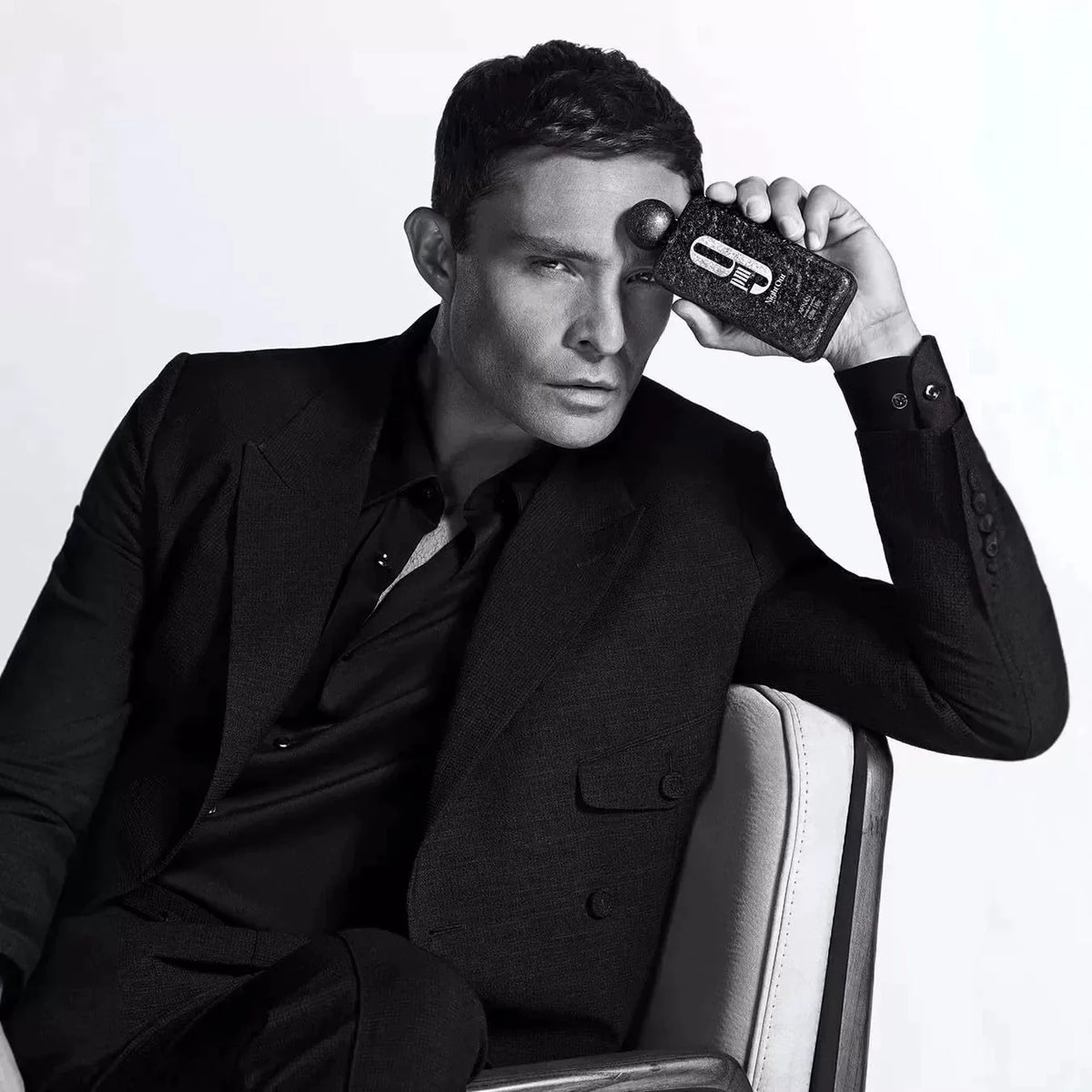 A man in a black suit holding a black perfume bottle.