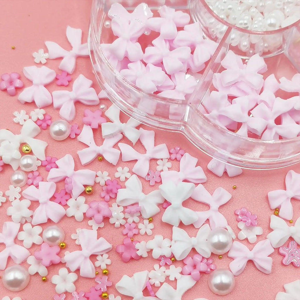 A close-up of various 3D nail art charms including bows, flowers, and pearls scattered around a storage container