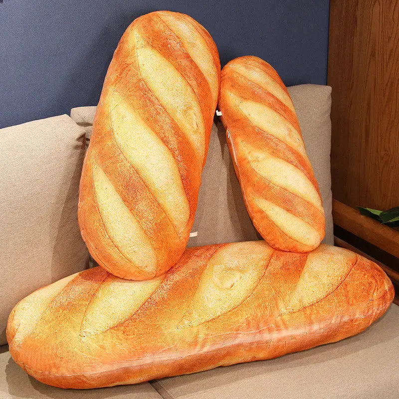 Three different sizes of plush baguette pillows arranged on a grey sofa.