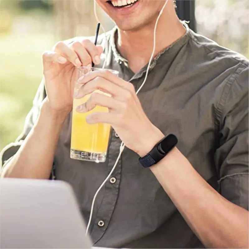 Person wearing a dark blue nylon watch band while holding a glass of orange juice