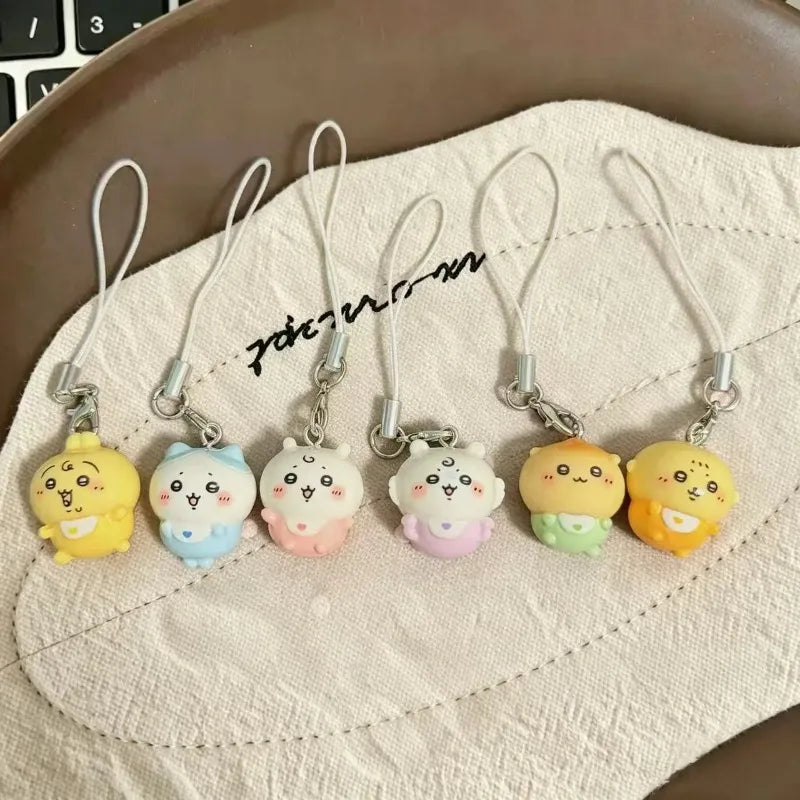 A group of six small character phone charms with lanyards arranged on a textured cloth.