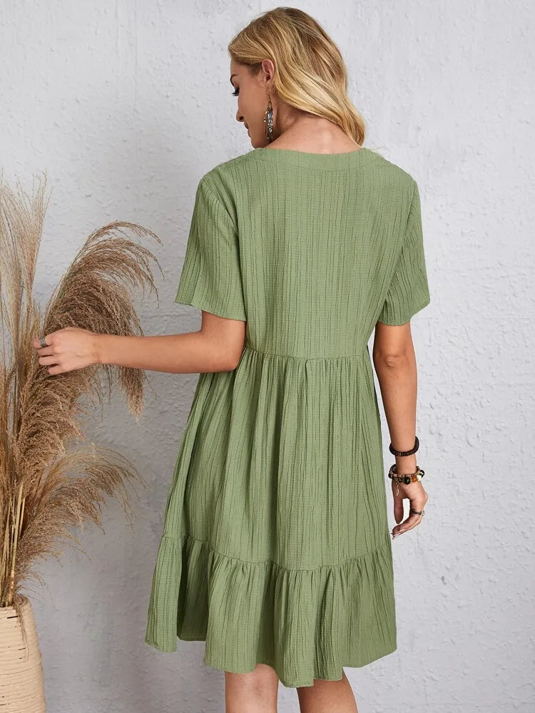 A woman seen from the back wearing a short-sleeved green V-neck textured mini dress with a tiered ruffle hem.