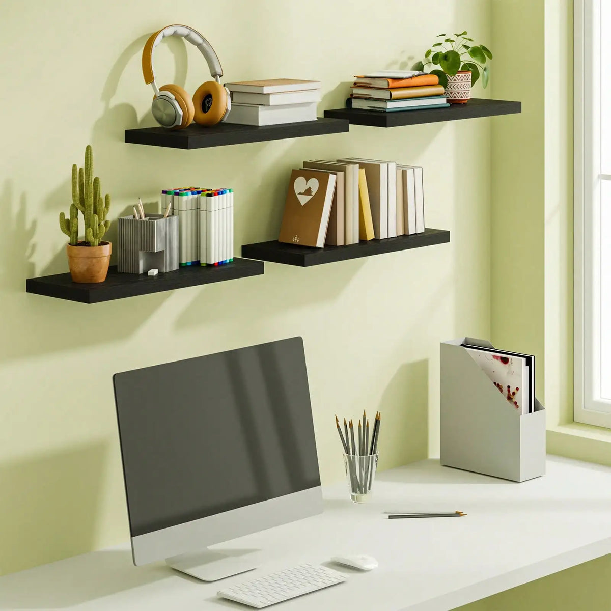 Four black floating shelves installed on a light green wall above a desk with a computer, holding books and decor
