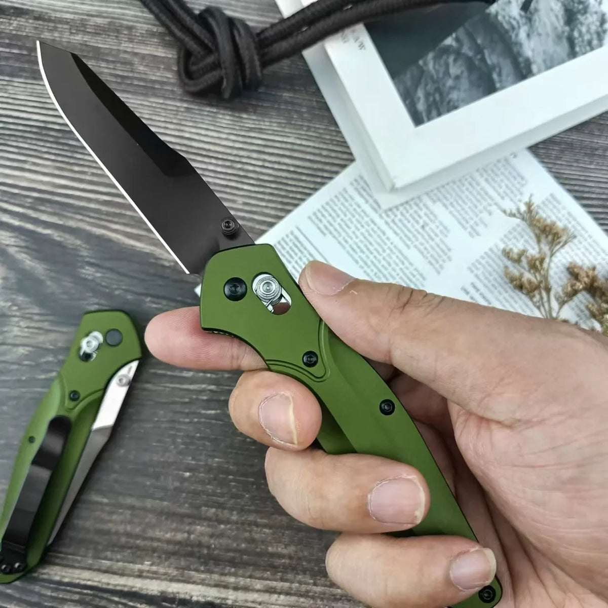 A hand holding an olive green folding knife with a black blade.