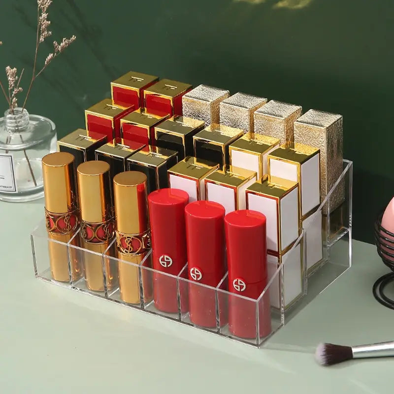 A clear acrylic 24-grid lipstick storage display filled with various high-end lipsticks on a green table