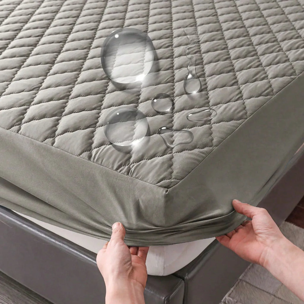 A grey quilted waterproof mattress protector being placed on a bed with water droplets on the surface