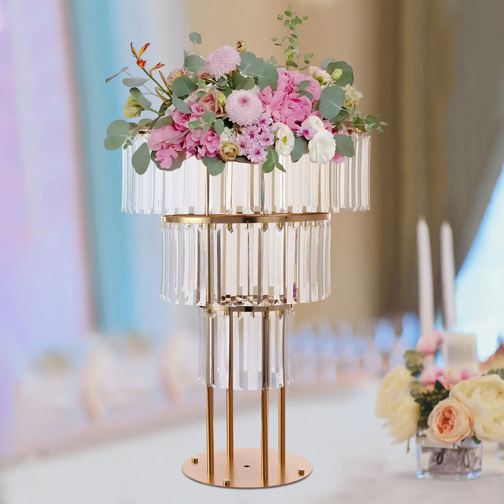 A three-tier gold metal and crystal flower stand decorated with a floral centerpiece on a table.