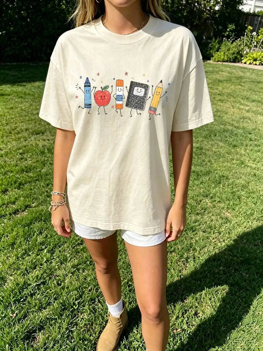 A person wearing a cream-colored t-shirt with a school supplies graphic standing in a grassy area.
