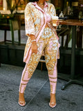 A woman wearing a pink and gold ornate print two-piece shirt and pants set, holding a coffee cup.
