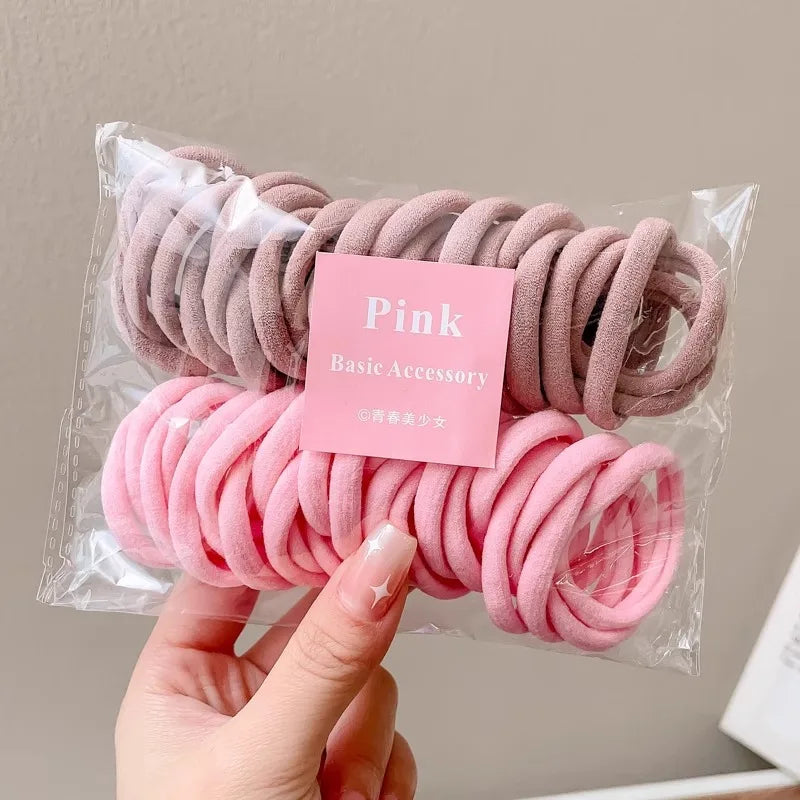 Hand holding a transparent plastic bag containing shades of pink nylon hair ties with a pink label.