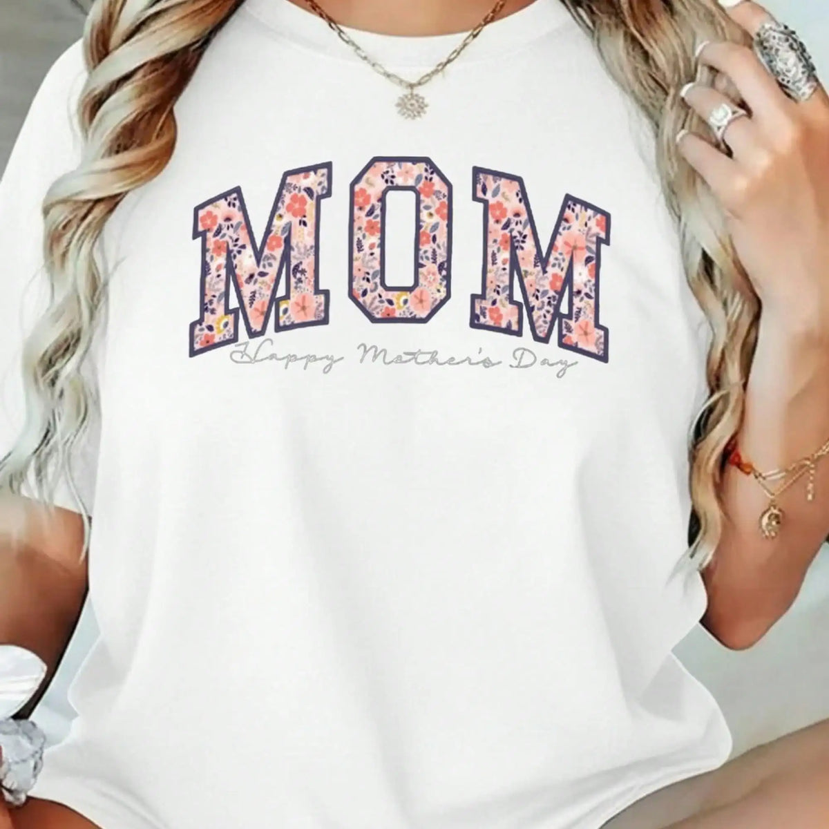 A woman wearing a white round-neck t-shirt with a floral MOM graphic and Happy Mother's Day text.