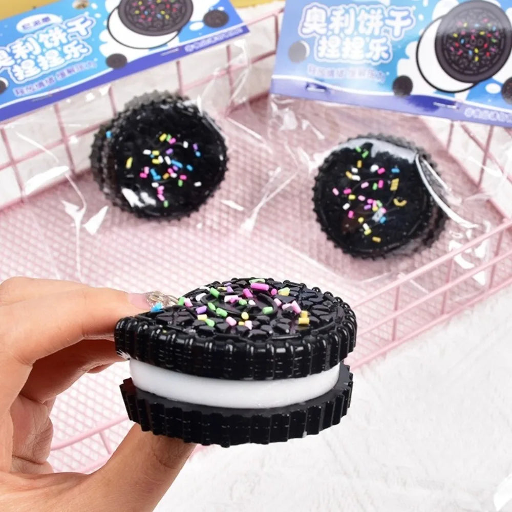 A black and white cookie-shaped stress relief squishy toy held in hand with packaged items in the background.