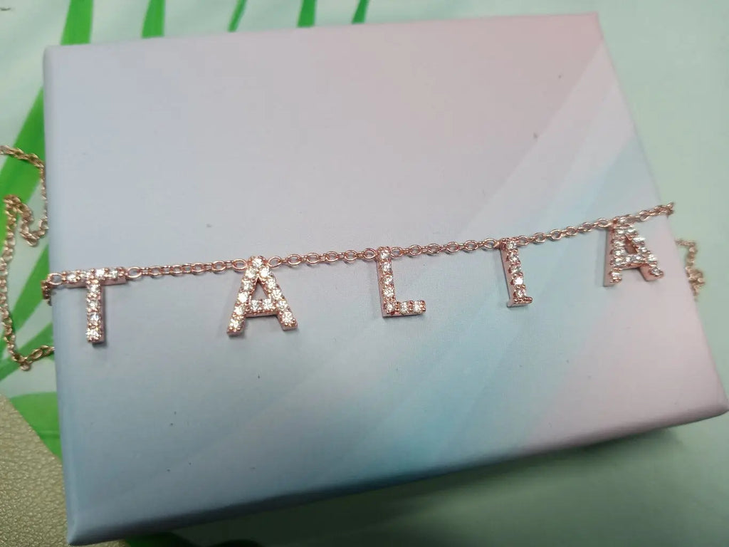 Rose gold letter necklace with crystals resting on a light blue gift box