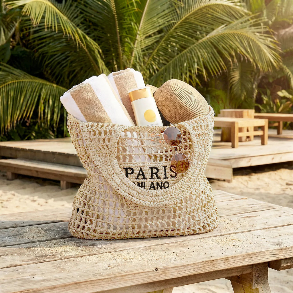 A beige woven mesh beach bag filled with towels and sunscreen on a wooden table at the beach.