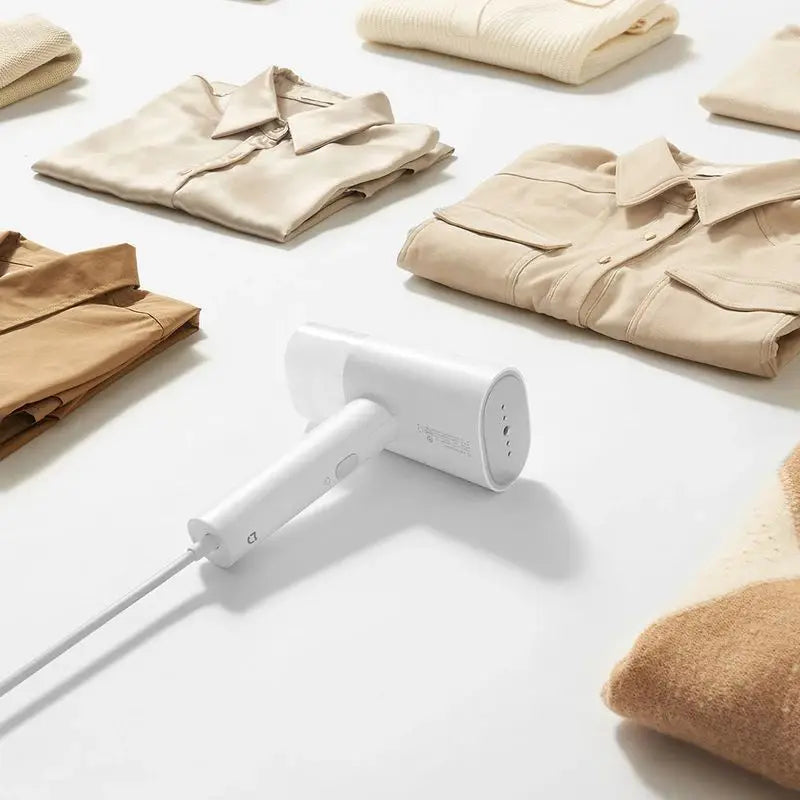 White handheld garment steamer placed on a surface with neatly folded clothes.
