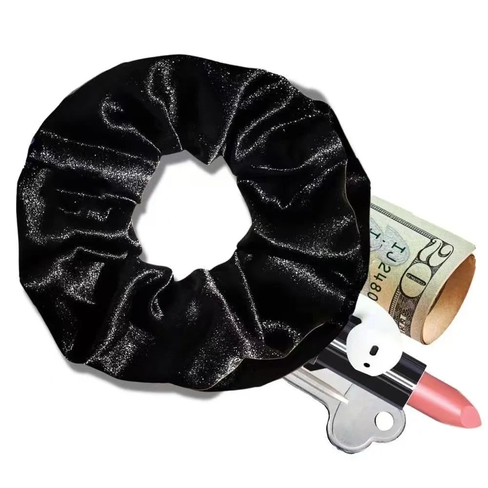 A single black velvet hair scrunchie with a zipper pocket containing cash, a lipstick, a key, and a wireless earbud.