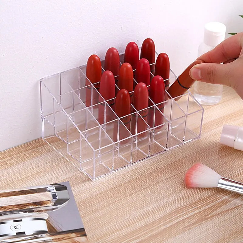 A clear acrylic lipstick storage rack being filled by a hand, holding various shades of lipstick