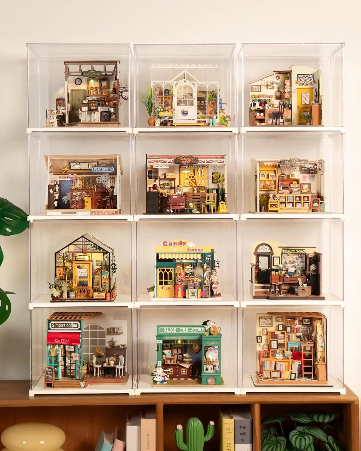 Twelve clear acrylic display cases stacked in a 3x4 grid, each containing different miniature room models
