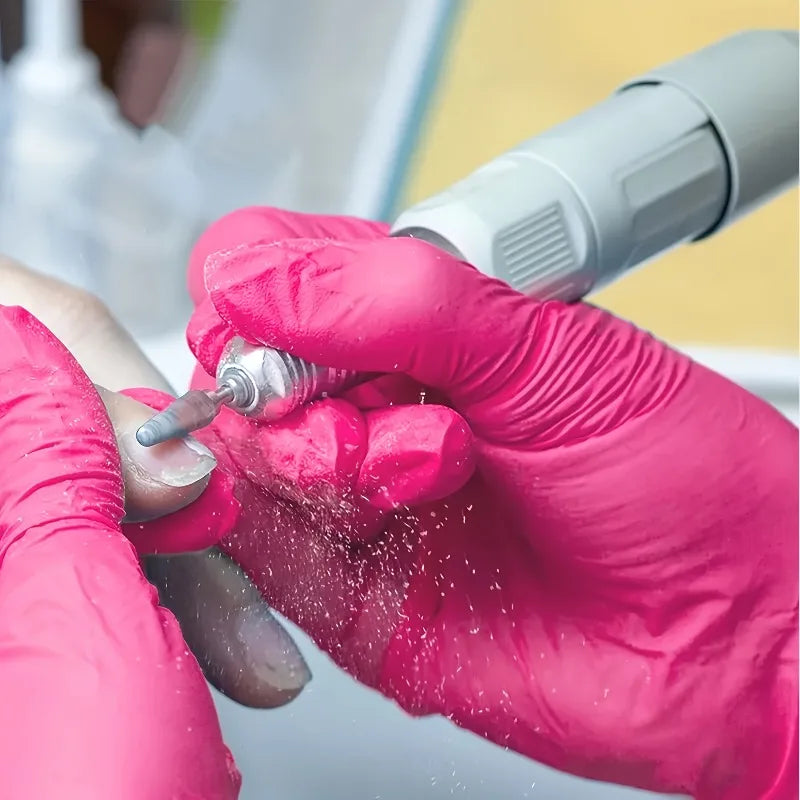 Close up of hands in rose red nitrile gloves using a nail drill tool