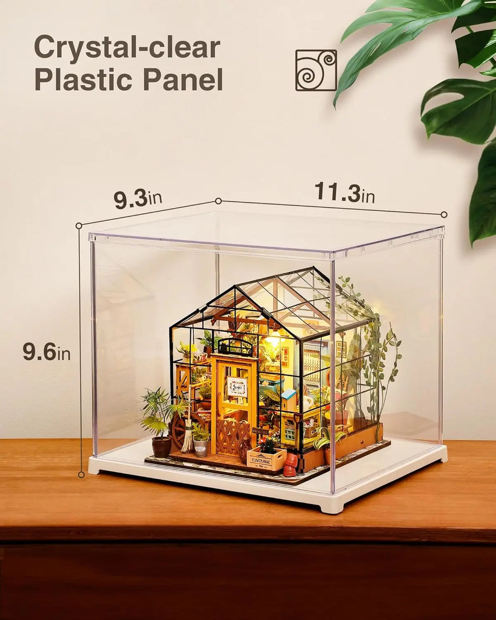 Clear acrylic display case containing a miniature greenhouse model on a wooden surface